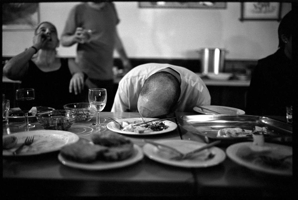 Schwarz-weiss Fotografie von einem Mann. Er wirkt satt vor Essen und hat den Kopf auf den Tisch gelegt.